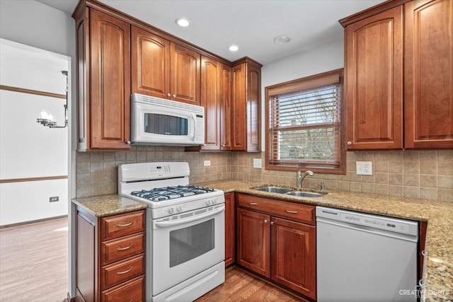 kitchen featuring backsplash, light stone countertops, light wood-type flooring, white appliances, and a sink