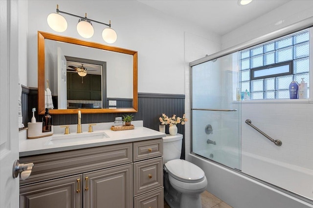 full bathroom featuring toilet, a wainscoted wall, enclosed tub / shower combo, tile patterned flooring, and vanity