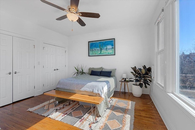 bedroom with a ceiling fan, baseboards, two closets, and wood finished floors