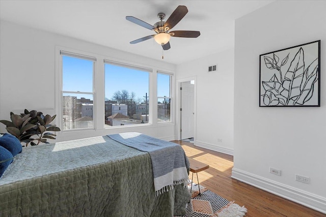 bedroom with ceiling fan, wood finished floors, visible vents, and baseboards