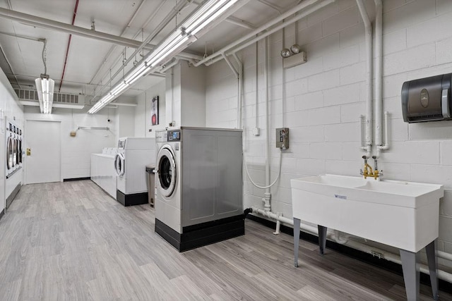 laundry room featuring a sink, concrete block wall, light wood-type flooring, and washer and clothes dryer