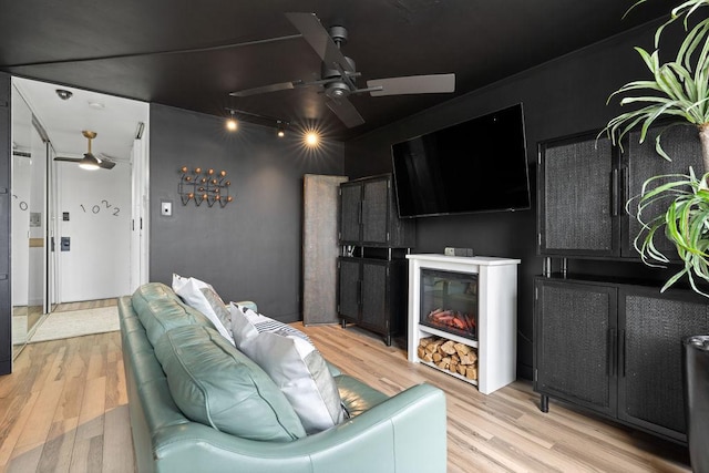 cinema with a glass covered fireplace, a ceiling fan, and light wood finished floors