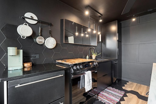 kitchen with backsplash, black gas stove, dark stone countertops, wood finished floors, and a sink