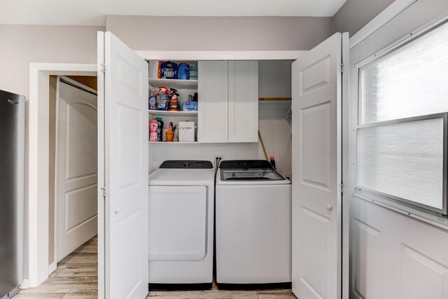 clothes washing area featuring light wood finished floors, washing machine and dryer, and cabinet space