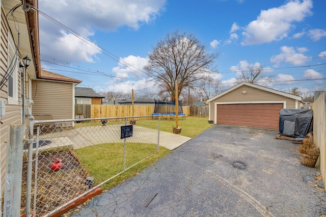 view of yard featuring fence private yard, an outdoor structure, a detached garage, a trampoline, and a patio area