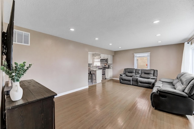 living area featuring baseboards, a textured ceiling, visible vents, and light wood-style floors