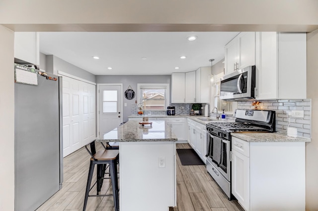 kitchen with stainless steel appliances, white cabinetry, light stone counters, and a kitchen bar