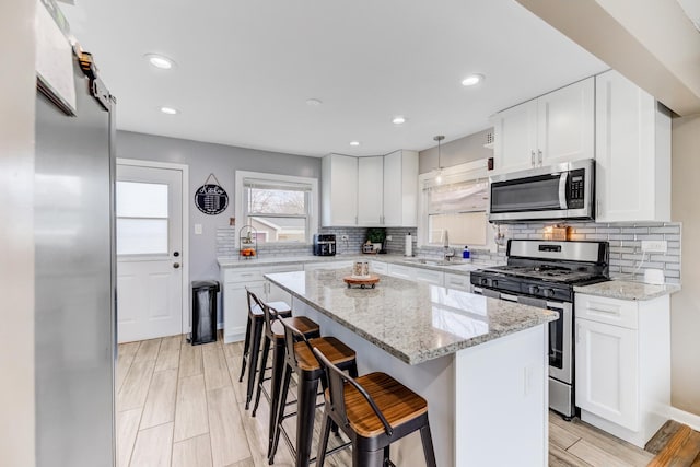 kitchen with white cabinets, a breakfast bar area, appliances with stainless steel finishes, a center island, and a sink