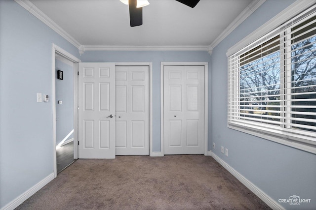 unfurnished bedroom with carpet floors, ornamental molding, baseboards, and two closets