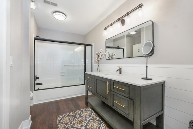 full bathroom featuring visible vents, wainscoting, wood finished floors, enclosed tub / shower combo, and vanity