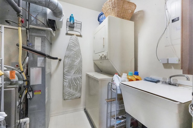 laundry area featuring tile patterned floors, stacked washer and dryer, a sink, heating unit, and baseboards