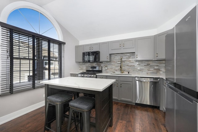 kitchen featuring dark wood-type flooring, vaulted ceiling, gray cabinets, appliances with stainless steel finishes, and a sink