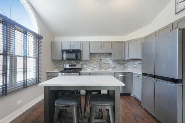 kitchen with gray cabinets, a sink, dark wood finished floors, stainless steel appliances, and decorative backsplash