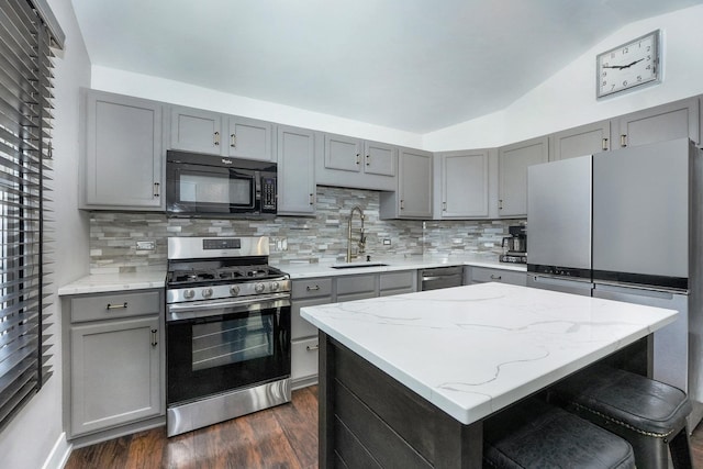 kitchen featuring gray cabinetry, a sink, backsplash, stainless steel appliances, and vaulted ceiling