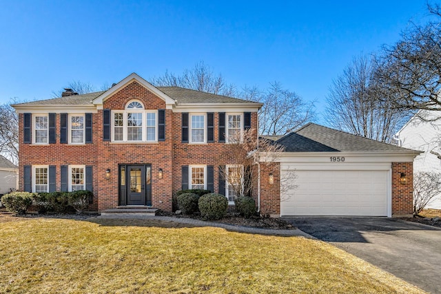 colonial house with a garage, a shingled roof, brick siding, driveway, and a front lawn