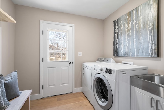 clothes washing area featuring light wood finished floors, cabinet space, baseboards, and washer and dryer