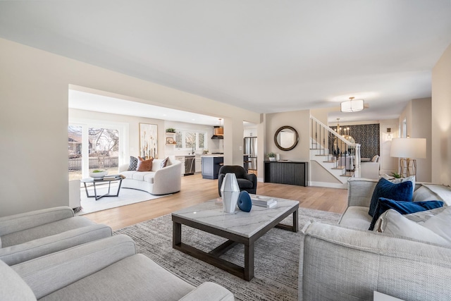 living area featuring light wood-style flooring, a notable chandelier, stairway, and baseboards