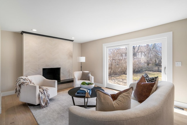 living area with recessed lighting, baseboards, a tiled fireplace, and wood finished floors