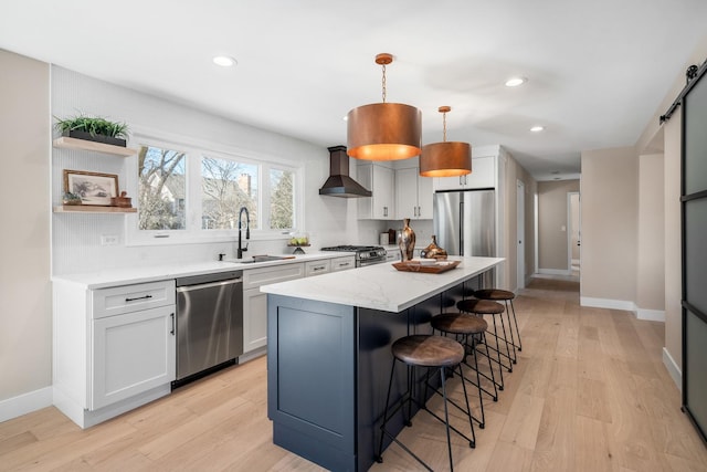 kitchen featuring appliances with stainless steel finishes, a sink, wall chimney range hood, light wood-type flooring, and a kitchen breakfast bar