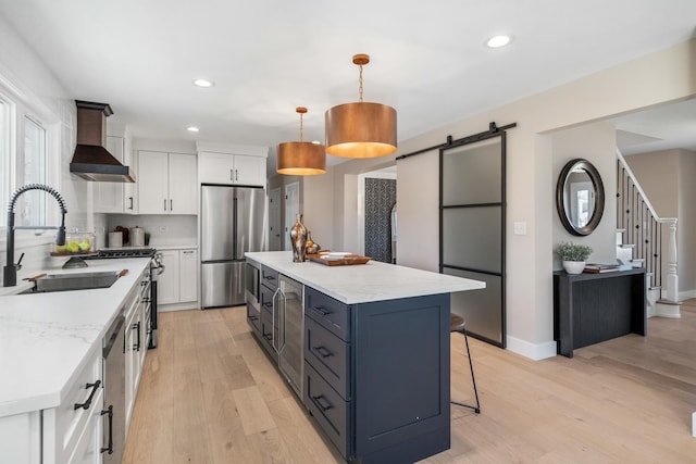 kitchen featuring appliances with stainless steel finishes, white cabinets, wall chimney exhaust hood, and a barn door