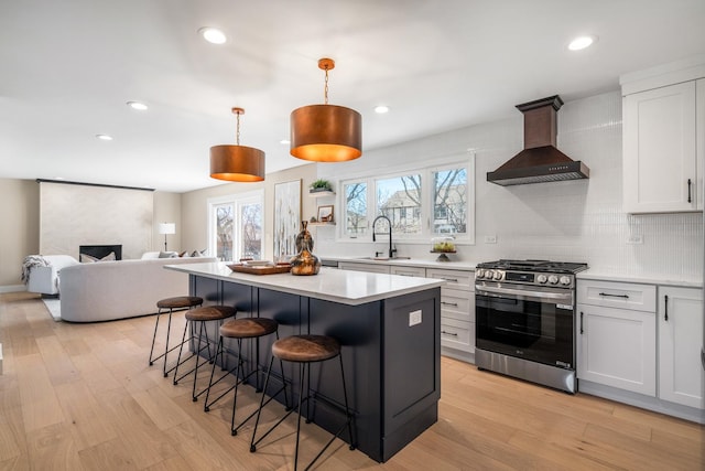 kitchen featuring a breakfast bar, light wood-style flooring, stainless steel range with gas stovetop, a sink, and wall chimney range hood