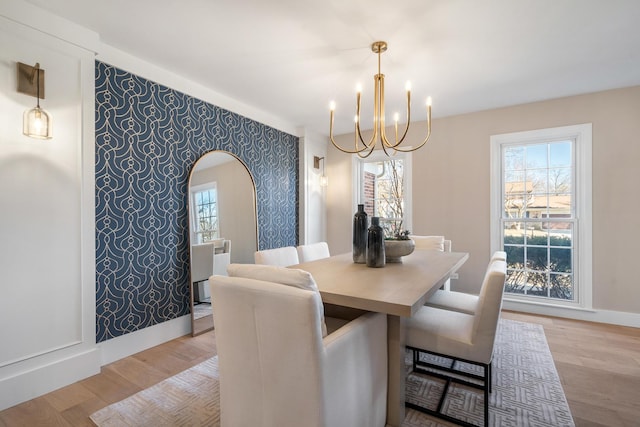 dining room featuring arched walkways, light wood finished floors, an accent wall, baseboards, and wallpapered walls