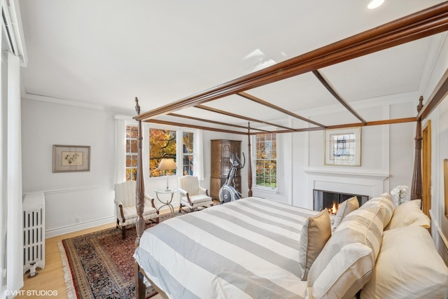 bedroom with light wood-style floors, radiator, crown molding, and a warm lit fireplace
