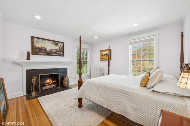 bedroom featuring crown molding, radiator heating unit, wood finished floors, and a fireplace with flush hearth