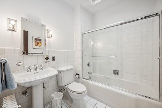 bathroom featuring toilet, wainscoting, combined bath / shower with glass door, tile walls, and tile patterned floors