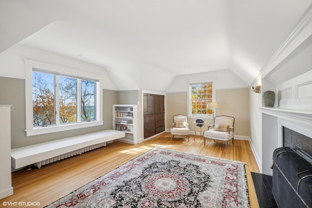 sitting room featuring a fireplace with flush hearth, lofted ceiling, baseboards, and wood finished floors