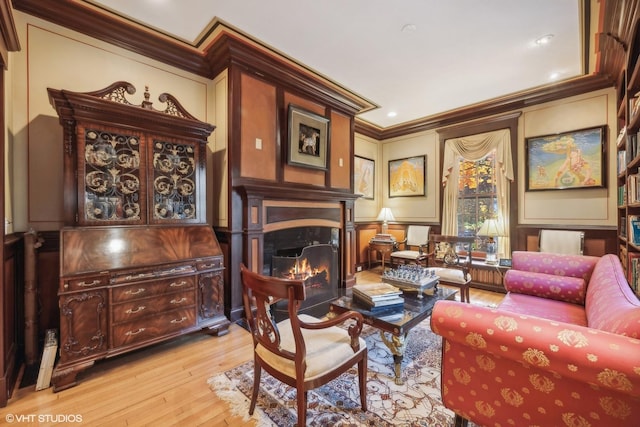 sitting room featuring a lit fireplace, a decorative wall, wood-type flooring, and ornamental molding