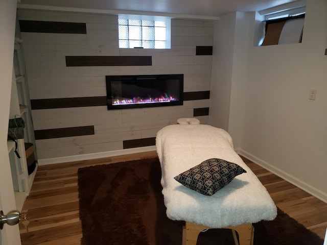 bedroom with a glass covered fireplace, wood walls, wood finished floors, and baseboards