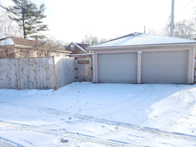 snow covered garage with a detached garage and fence