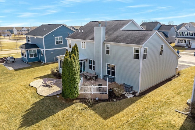 rear view of property featuring a lawn, a patio, a residential view, roof with shingles, and a chimney