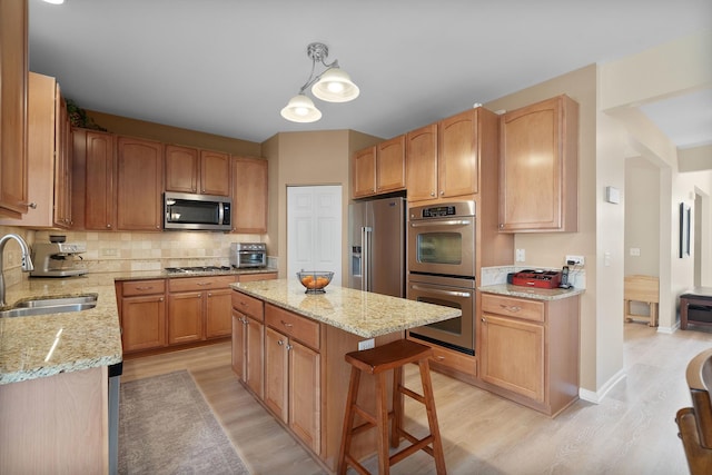 kitchen with light stone counters, appliances with stainless steel finishes, light wood-type flooring, and a sink