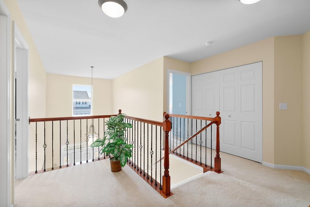 hall with baseboards, carpet, and an upstairs landing