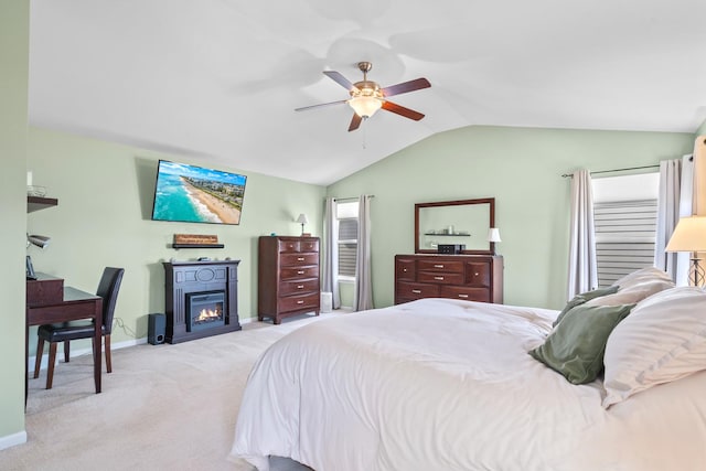 bedroom featuring lofted ceiling, a ceiling fan, a glass covered fireplace, baseboards, and light colored carpet