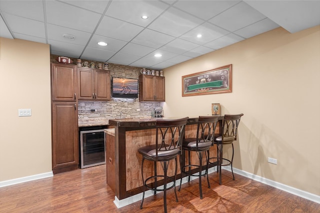 bar featuring decorative backsplash, wood finished floors, wine cooler, indoor wet bar, and baseboards