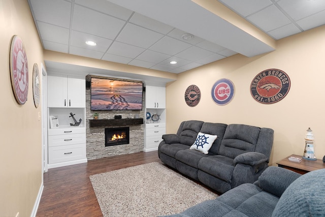 living area featuring baseboards, recessed lighting, a drop ceiling, dark wood-type flooring, and a glass covered fireplace