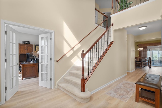 staircase with french doors, a high ceiling, baseboards, and wood finished floors