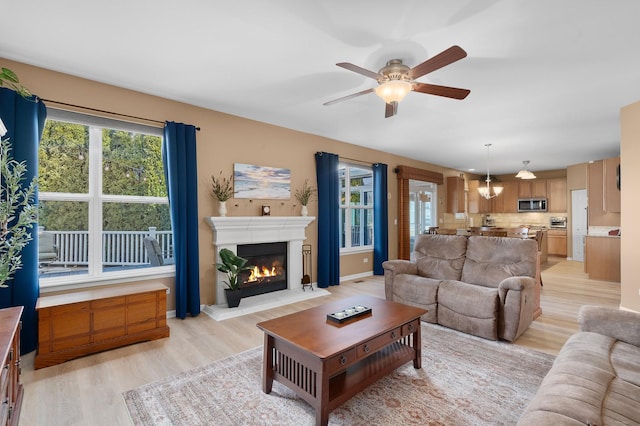 living area with a glass covered fireplace, baseboards, light wood-type flooring, and ceiling fan