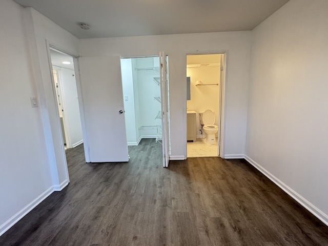 unfurnished bedroom with a closet, dark wood finished floors, connected bathroom, and baseboards