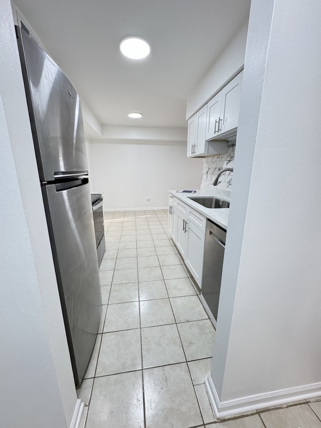 kitchen with light tile patterned floors, tasteful backsplash, appliances with stainless steel finishes, white cabinetry, and a sink