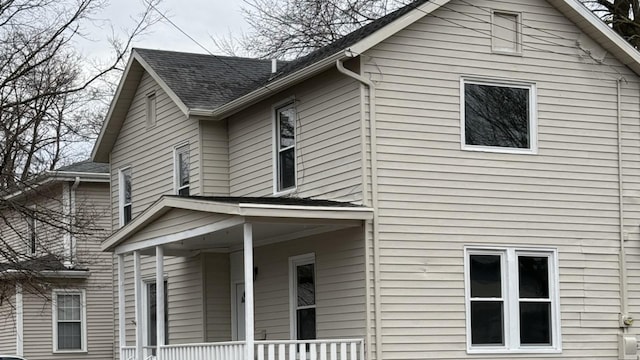 view of side of home featuring covered porch and roof with shingles