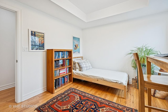 sitting room with baseboards, a raised ceiling, and light wood-style flooring