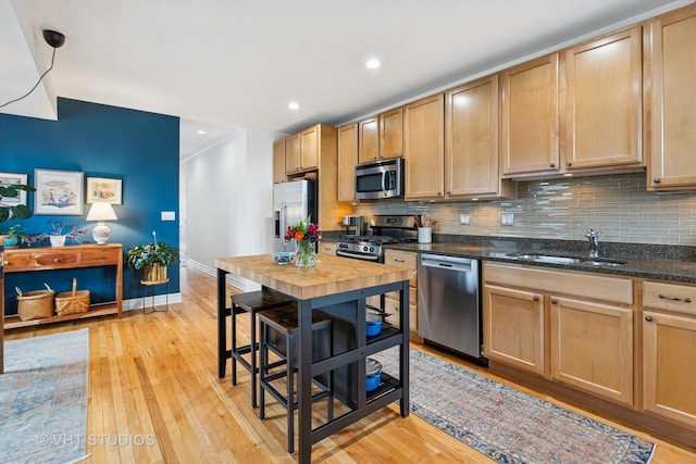 kitchen featuring light wood-style flooring, light brown cabinets, a sink, backsplash, and appliances with stainless steel finishes