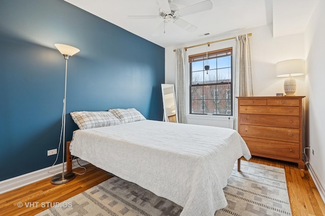 bedroom featuring visible vents, ceiling fan, baseboards, and wood finished floors