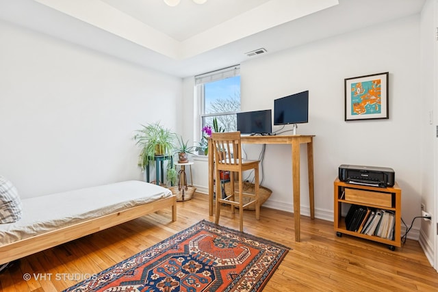 office space featuring visible vents, baseboards, a tray ceiling, and wood finished floors