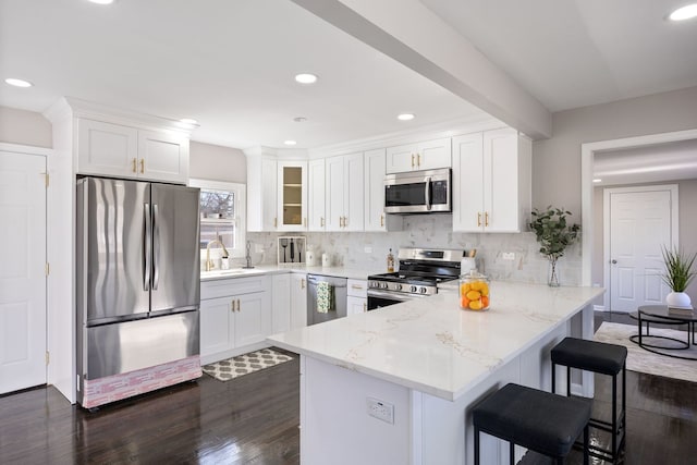 kitchen with a peninsula, white cabinets, stainless steel appliances, and backsplash