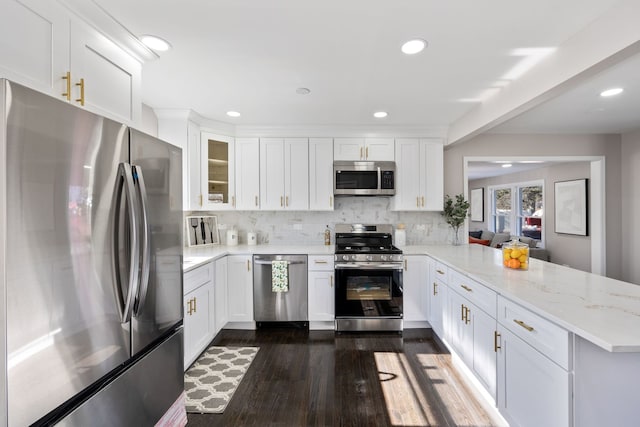 kitchen with white cabinets, dark wood-style flooring, a peninsula, stainless steel appliances, and backsplash